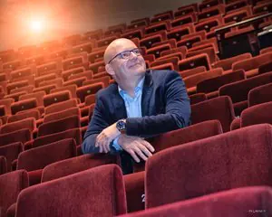 Gert-Jan Jansen zit alleen in een lege theaterzaal met rode stoelen